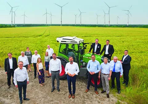 Fendt e100 Vario steht hinter einer Gruppe von Menschen mit Hintergrund von Windkraftwerken