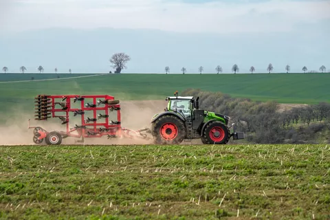 Seitenansicht des Fendt 1000 Vario mit eingeklappten Anbaugerät auf einem Feld