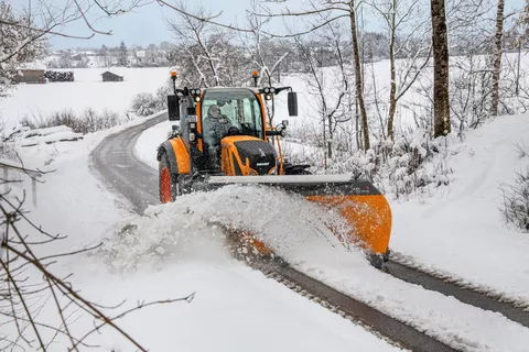 Orangener Fendt Traktor räumt Schnee auf einer Straße in einer verschneiten Landschaft