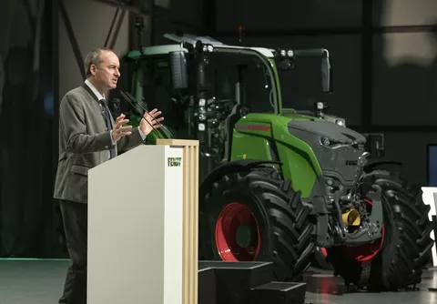 Ein Mann hält einen Vortrag vor Publikum. Im Hintergrund steht ein Fendt Traktor