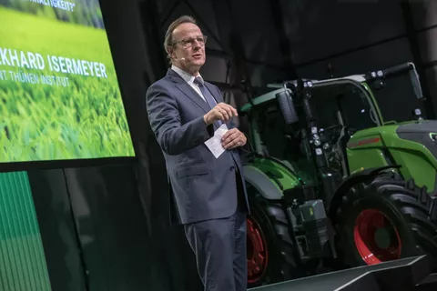 Ein Mann hält einen Vortrag vor Publikum. Im Hintergrund steht ein Fendt Traktor