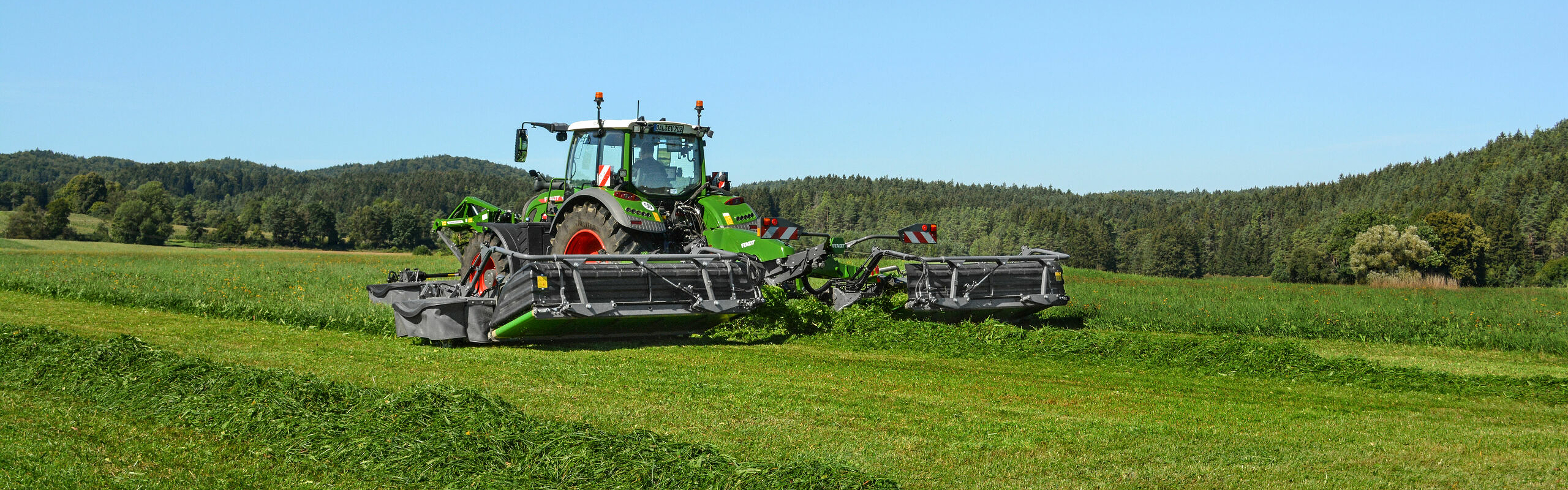 Ein grüner Fendt Traktor im Feld mit angehängter Mähkombination