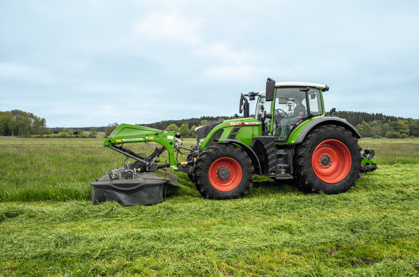 Seitenansicht eines grünen Fendt Traktor mit Direktanbau am Fronthubwerk auf der Wiese.