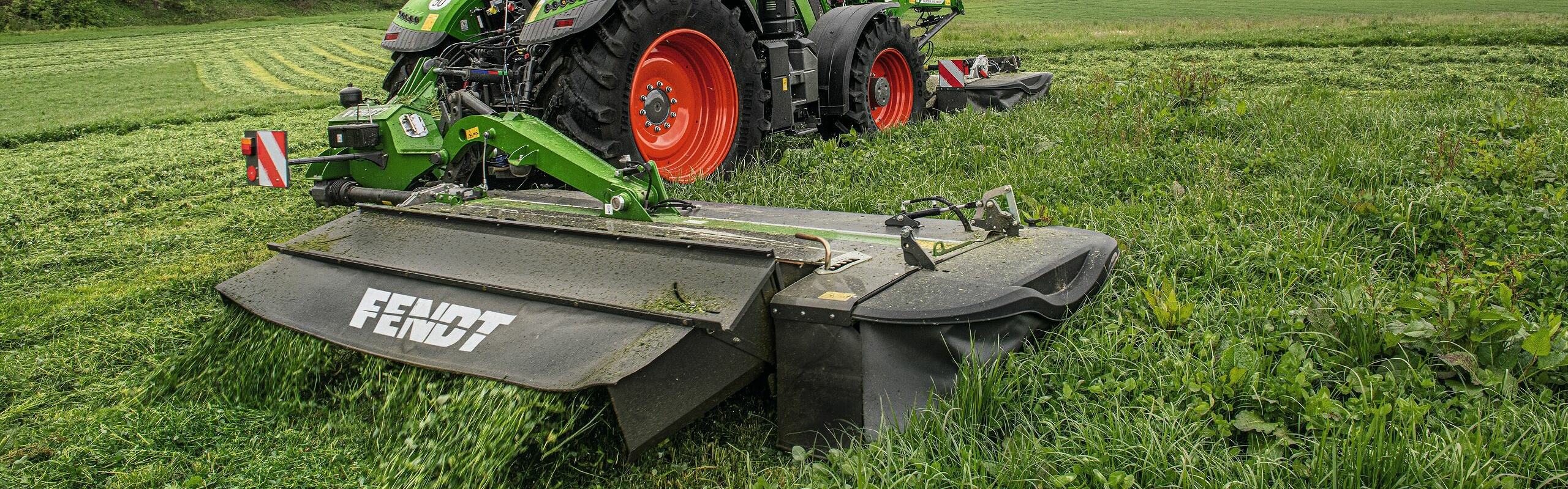 Ein Fendt 700 Vario mit einem Slicer Frontanbau und Heckanbau auf der rechten Seite im Grünland.