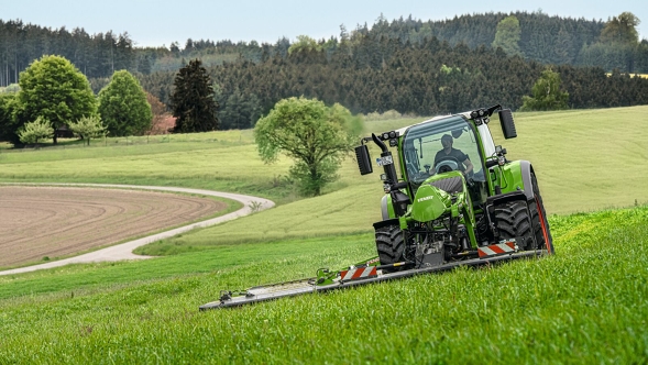 Ein Landwirt mäht mit einem Fendt Slicer Frontmähwerk eine grüne Wiese.