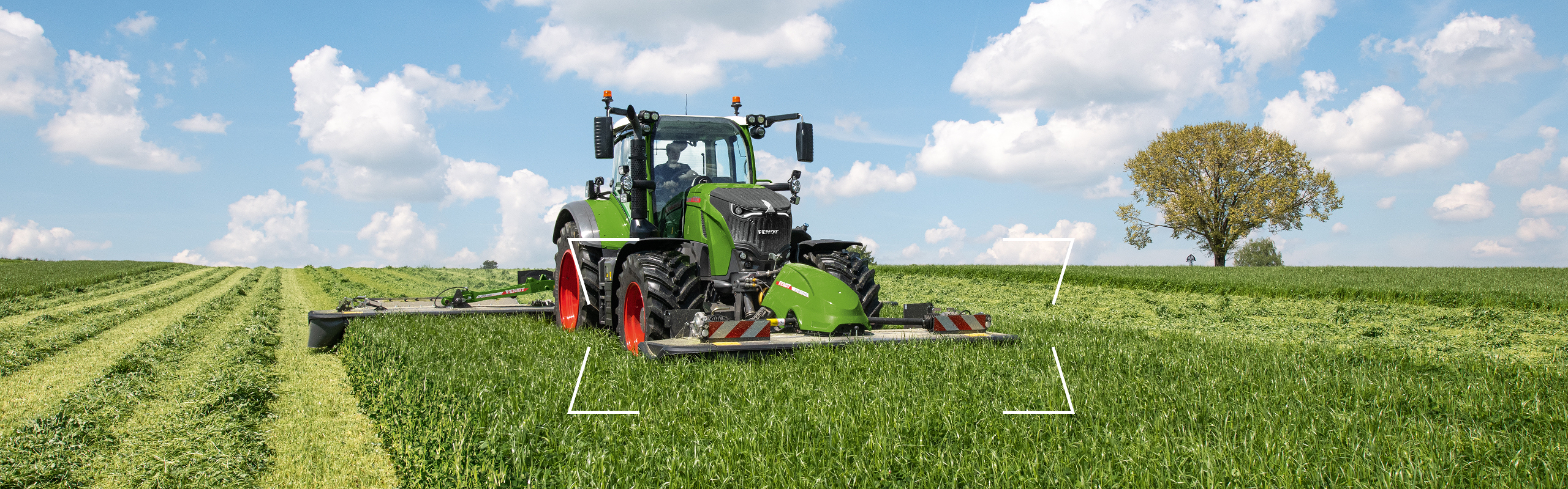 Ein Landwirt fährt mit einem Fendt Traktor über eine grüne Wiese und mäht mit einem Fendt Slicer mit Front- und Heckmähwerk.