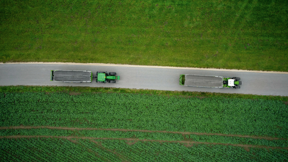 Ein Fendt 700 Vario Gen7 mit Ladewagen fährt vor einem John Deere Traktor mit Ladewagen.