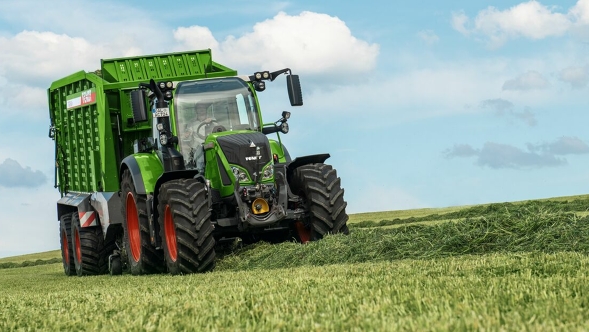 Ein Landwirt fährt mit einem Fendt 700 Vario Gen6 und einem Fendt Tigo Ladewagen auf die Wiese und lädt das Gras auf.