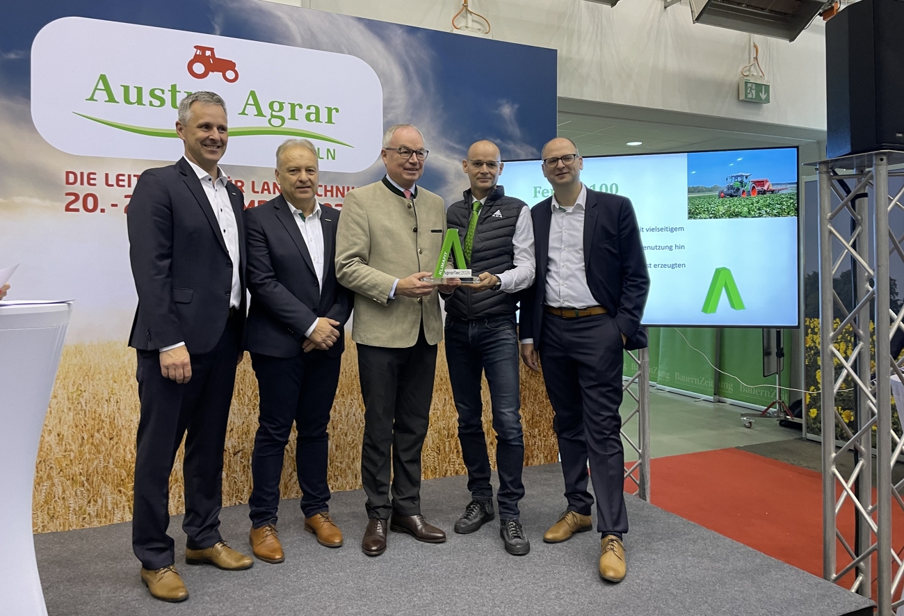 Übergabe des AgrarTec Klimafit 2024 für den Fendt  e100 Vario durch Heinrich Prankl an das Fendt Österreich Team mitGeorg Herbig, Kurt Wipfler und Eward Snieder sowie Roman Roth von der ACA GmbH, alleHerren stehen auf einer Bühne vor einer Leinwand