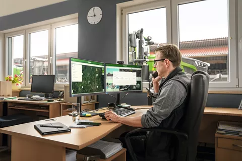 Man sitting at desk in front of FendtONE web application and Fendt tractors in background