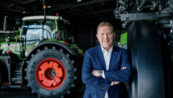 Christoph Gröblinghoff está de pé em um terno azul escuro com os braços cruzados entre um trator Fendt e um pulverizador de campo Fendt Rogator.