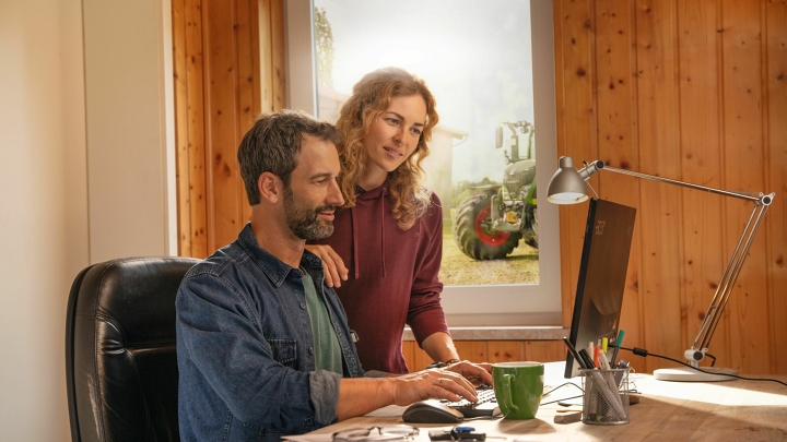 Um casal de agricultores verifica sua troca automatizada de dados por meio da agronomia Smart Farming Fendt em um PC