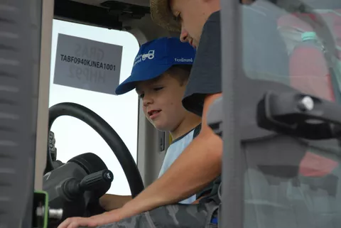 Ein kleiner Junge darf auf dem Fahrersitz eines Traktors Platz nehmen