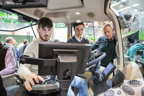 Drei männliche Personen sitzen auf dem Traktor und blicken interessiert zum Bildschirm