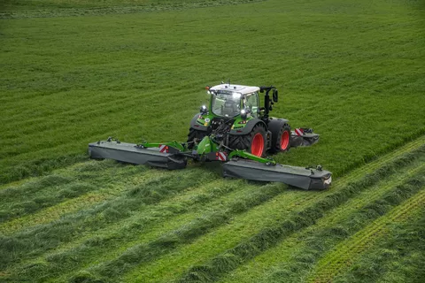 Fendt Traktor mäht bei eingeschaltetem Licht mit Fendt Slicer Front-Heckmähwerkkombination über Wiese