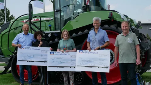 Fünf Personen stehen mit 3 Schecks in der Hand vor einem Fendt 943 Vario Raupentraktor