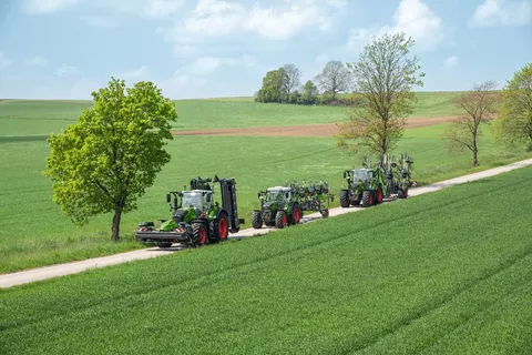 Drei Traktoren fahren hintereinander auf einem Feldweg. Rechts und links sind Felder und Bäume