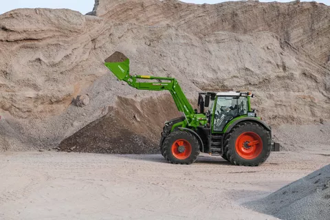 Ein Fendt Traktor mit Frontladerschaufel. Im Hintergrund ist ein Berg aus Kies und Sand.