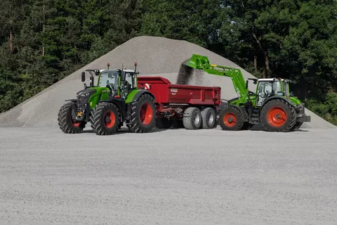 Ein Fendt Traktor lädt Kies auf einen roten Anhänger. Der Anhänger hängt an einem zweiten Fendt Traktor