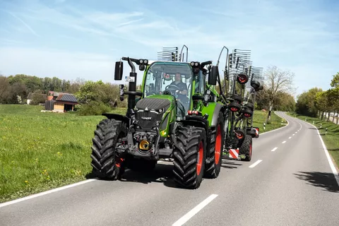 Ein Fendt Traktor mit einem angehängten Fendt Schwader fährt auf einer Landstraße.