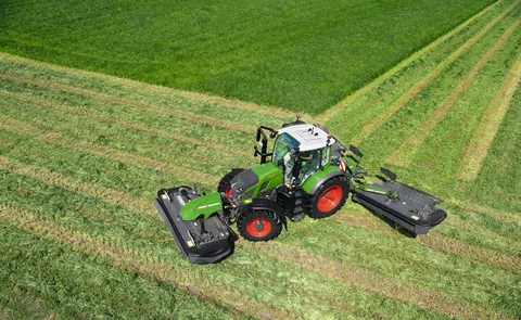 Ein Fendt Traktor mit einem Fendt Mähwerk steht auf einer grünen Wiese, die bereits zum Teil abgemäht wurde