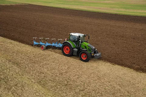 Ein Fendt Traktor pflügt ein Feld mit einem blauen Pflug.