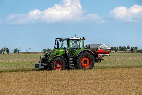 Ein Fendt Traktor fährt mit einem Kunstdüngerstreuer fährt über einen Acker mit Getreide