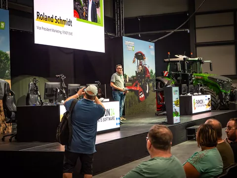 Roland Schmidt, Vice President Fendt Marketing EME, steht auf der FarmCon24 Bühne vor den Besucherinnen und Besuchern und begrüßt diese im Fendt Forum, im Hintergrund steht ein Fendt Traktor