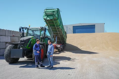 Zwei Männer vor einem Gespann mit Fendt 720 Vario und Hänger vor einer Halle mit Sand