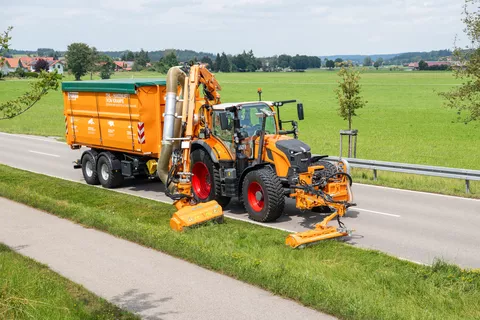 Fendt 728 Vario in kommunal-orange mit zwei Auslegemähern bei Mäharbeiten am Straßenrand und mit einem Anhänger