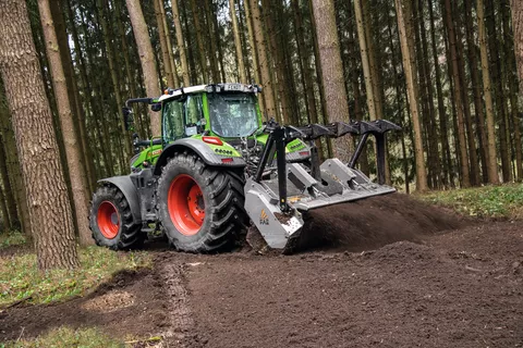 In einem Nadelwald arbeitet ein Fendt 700 Vario Gen7 mit einer Fräse am Heck