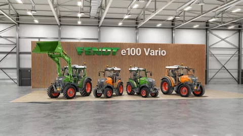 In einer Reihe vor einer Wand mit Holzlatten stehen 4 Modelle des Fendt e100 Vario, v.l. ein grüner Fendt e107 Vario mit Frontlader, ein Fendt e107 V Vario in kommunal-orange, daneben einer in grün, als Vierter ein Fendt e107 Vario in kommunal-orange