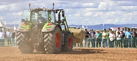 Ein Fendt Traktorlädt einen Strohballen mit dem Frontlader bei einer Fendtgüinos Vorführung im Hintergrund Zuschauer