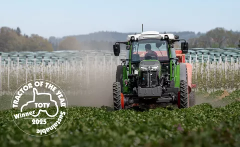 Fendte107 Vario auf einem Erdbeerfeld bei der Strohverteilung zwischen den Erdbeerreihen; unten links ist dasLogo für den Sustainable Tractor of the Year 2025 in weiß platziert