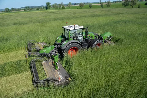 Ein Fendt Traktor fährt mit der Mähwerkskombination Fendt Slicer 960 KCB Pro durch hoch stehendes Gras im Grünland und mäht