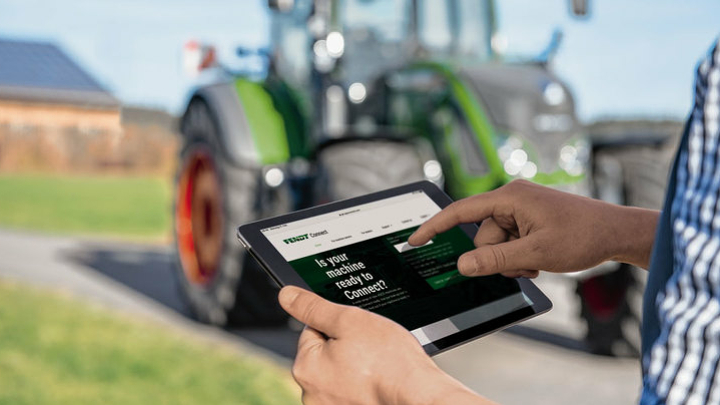 Tablet in zwei Händen gehalten zeigt Fendt-Connect. Im Hintergrund steht ein Fendt Traktor.