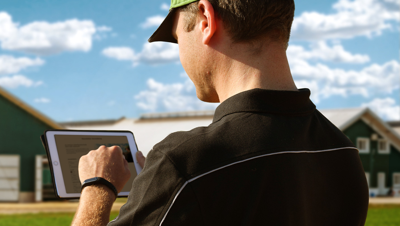 Ein Landwirt steht mit Tablet in der Hand vor seinem Hof und meldet sich für den Fendt Newsletter an