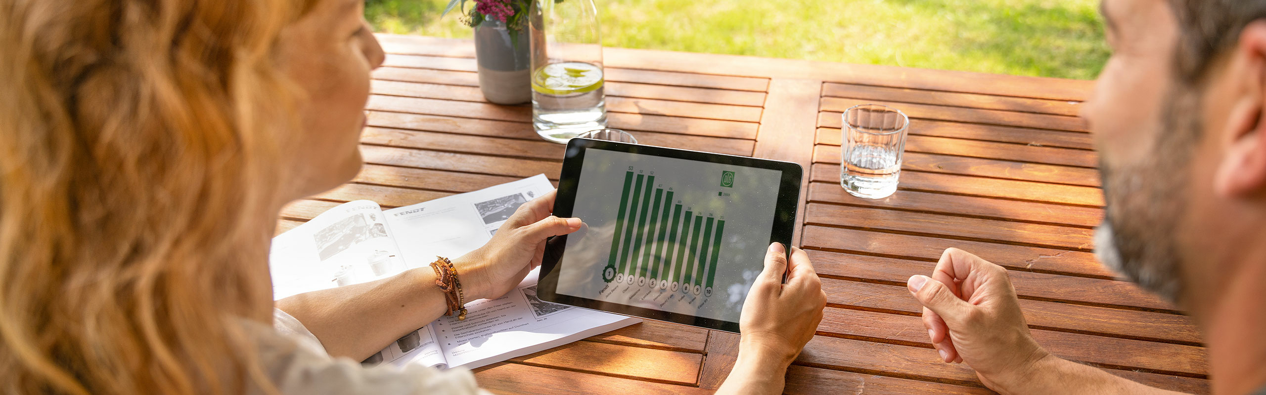 Eine Landwirtin und ein Landwirt sitzen am Gartentisch und schauen sich das Image-Barometer auf dem Tablet an.