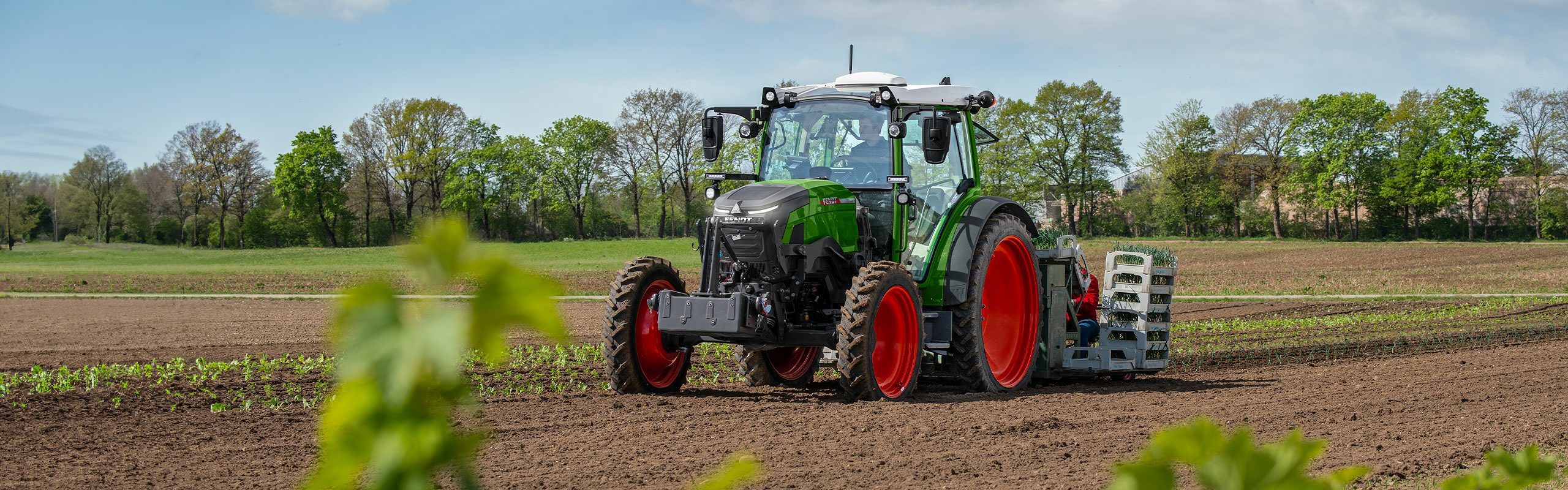 Ein grün lackierter Fendt e100 Vario mit roten Felgen bei der Feldarbeit