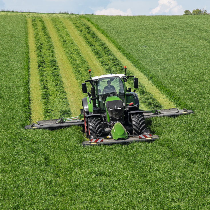 Ein Landwirt mäht mit einem Fendt Traktor und Fendt Slicer Frontmähwerk eine grüne Wiese.