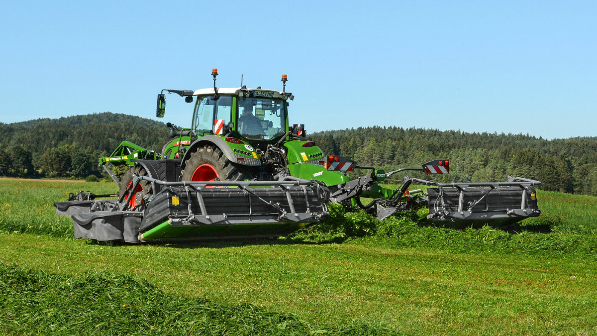 Ein Landwirt mäht mit einem Fendt Traktor und einer Fendt Mähkombination eine grüne Wiese.