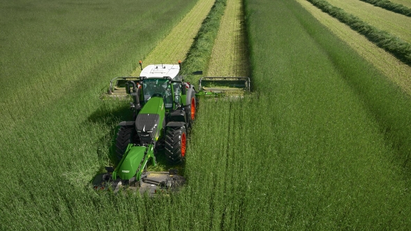 Aufnahme von oben wie ein Landwirt mit einem Slicer FQ und Slicer PRO-Mähkombination eine grüne hohe Wiese mäht.
