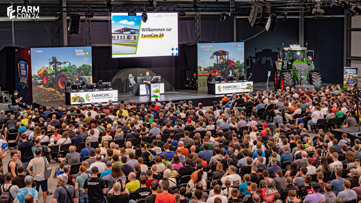 Besucherinnen und Besucher der FarmCon 24 schauen auf die Bühne und eine große Leinwand, wo sie einen ersten Einblick in den neuen Landwirtschafts-Simulator 2025 bekommen