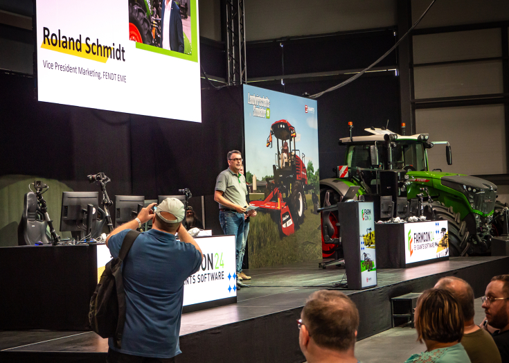 Roland Schmidt, Vice President Fendt Marketing EME, steht auf der FarmCon24 Bühne vor den Besucherinnen und Besuchern und begrüßt diese im Fendt Forum, im Hintergrund steht ein Fendt Traktor