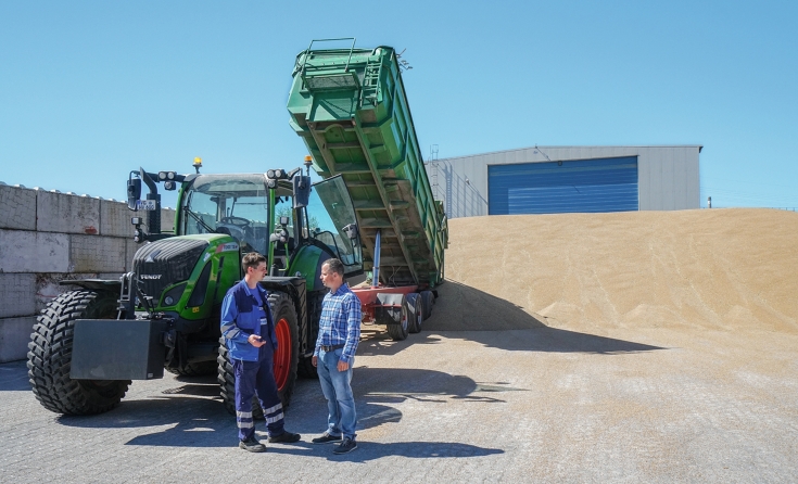 Zwei Männer vor einem Gespann mit Fendt 720 Vario und Hänger vor einer Halle mit Sand