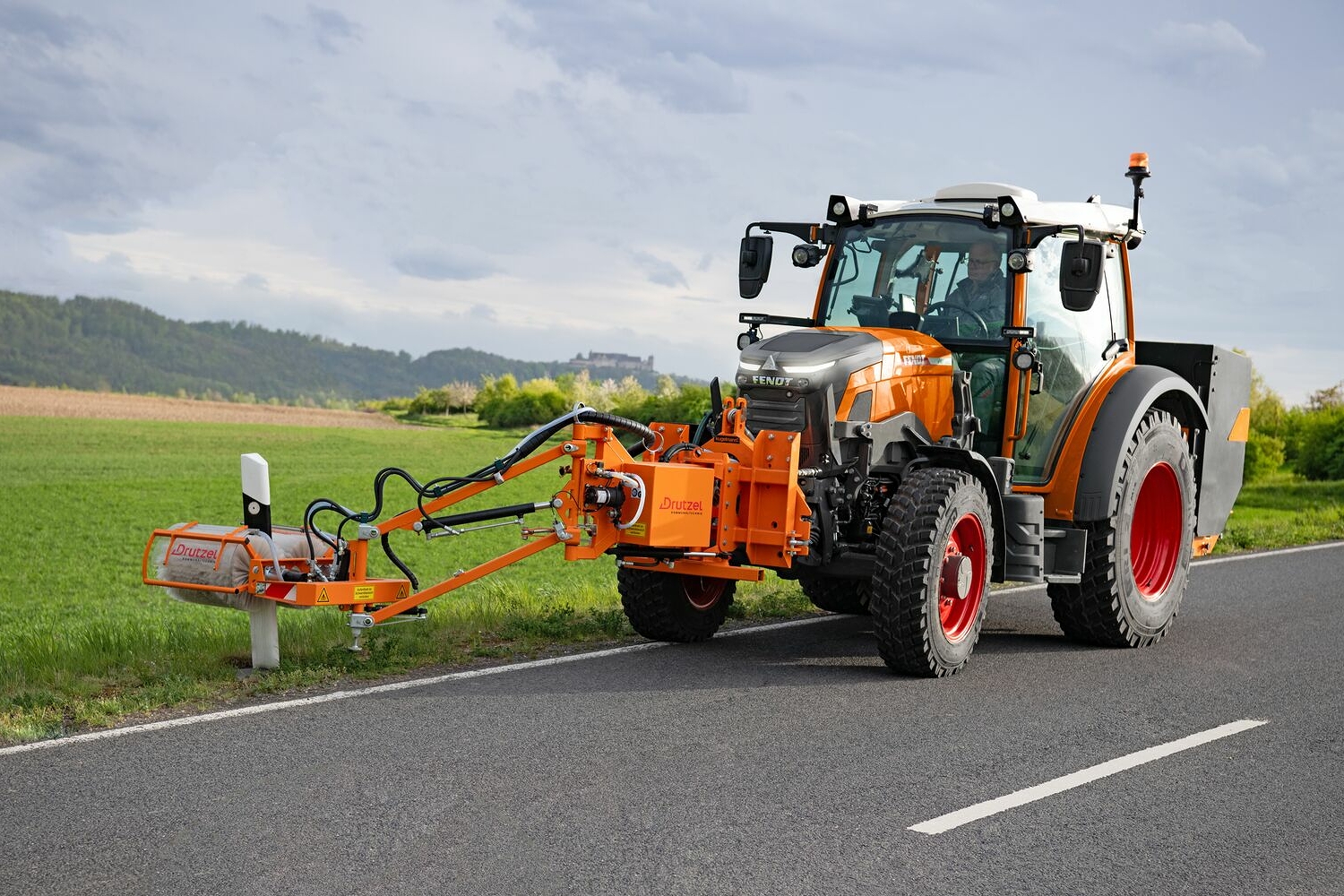 Der orange lackierte Fendt e100 Vario als ISU Maschine während eines Pylonen-Reinigungseinsatzes auf einer Landstraße