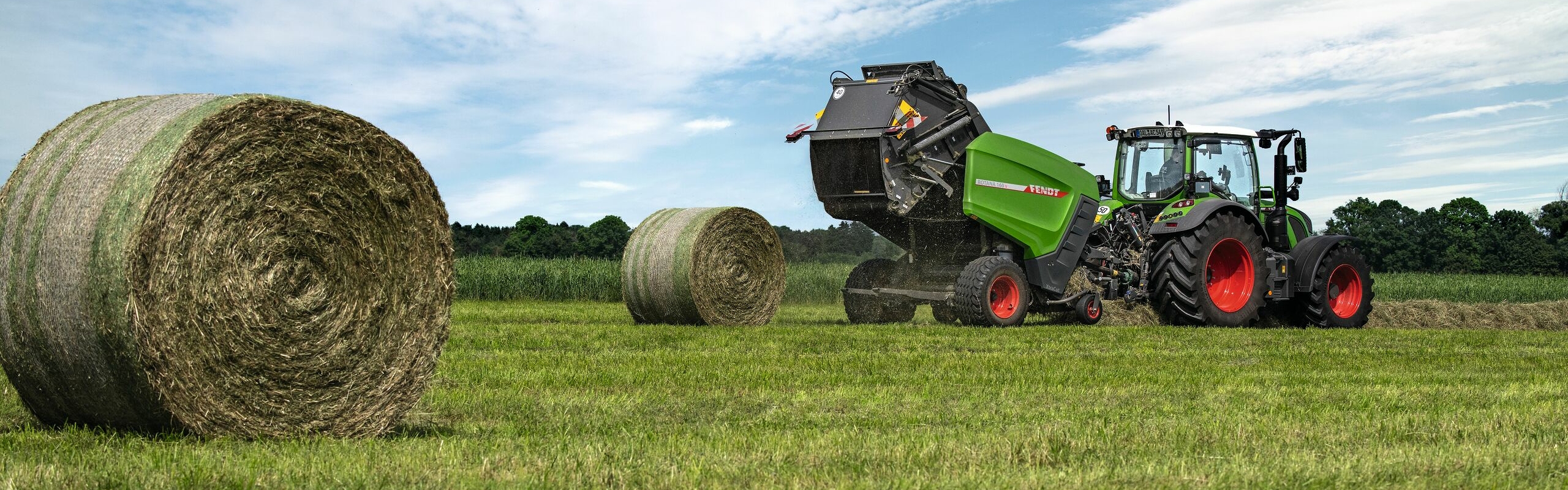 Die Fendt Rundballenpresse Rotana 160V hinter einem Fendt Traktor gespannt im Feldeinsatz, um Rundballen zu pressen