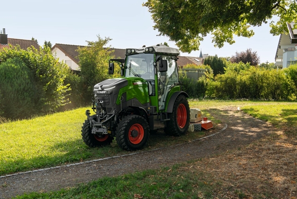 Ansicht eines Fendt e100 V Vario in Nature Green mit roten Felgen am Rand einer Ortschaft