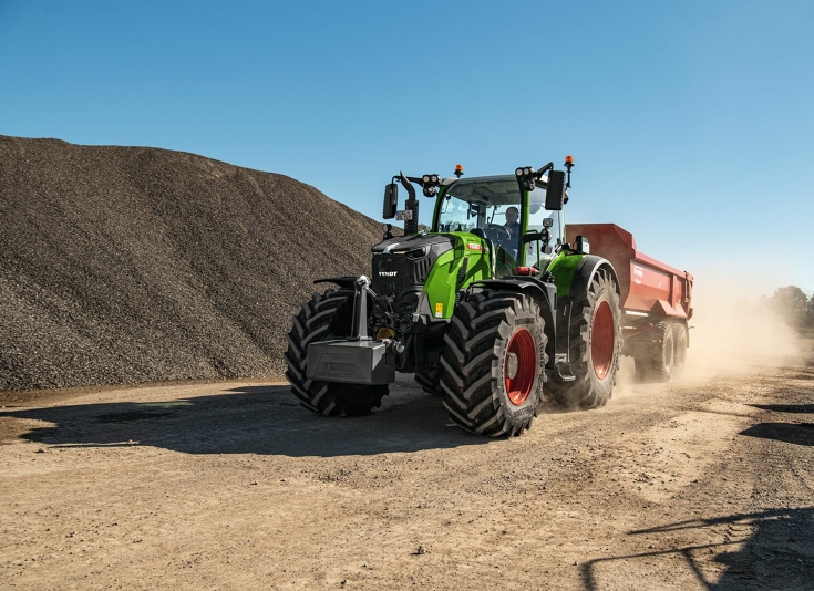 Ein Fendt 728 Vario fährt auf einer Baustelle mit einer roten Mulde an einem Berg aus Kies vorbei