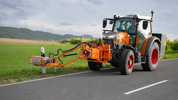 Der orange lackierte Fendt e100 Vario als ISU Maschine während eines Pylonen-Reinigungseinsatzes auf einer Landstraße